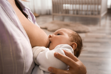 Photo of Young woman breast feeding her little baby at home, closeup