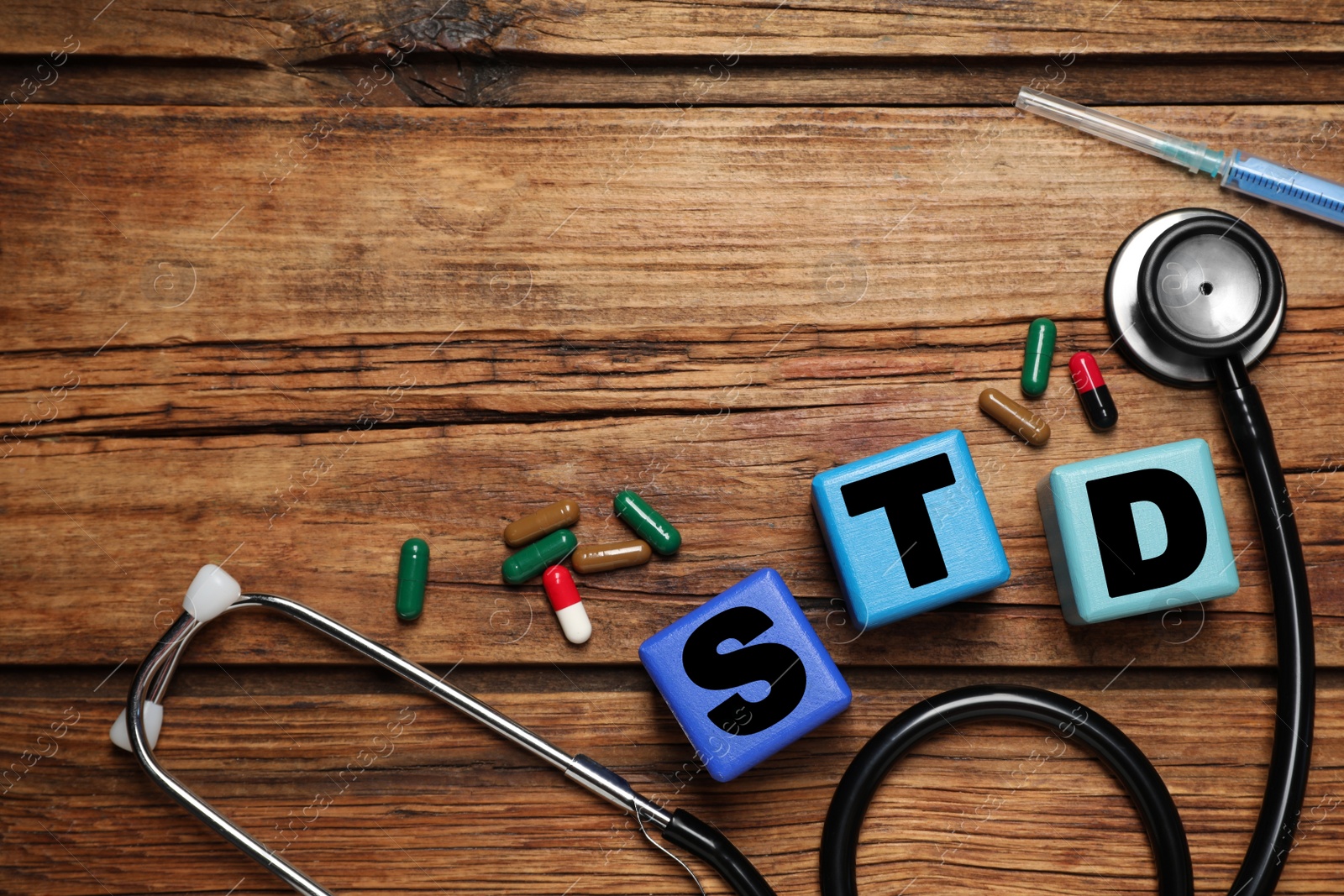 Photo of Colorful cubes with letters STD, capsules, stethoscope and syringe on wooden table, flat lay. Space for text