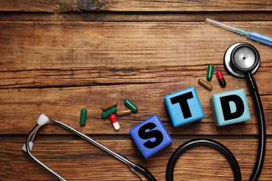 Colorful cubes with letters STD, capsules, stethoscope and syringe on wooden table, flat lay. Space for text