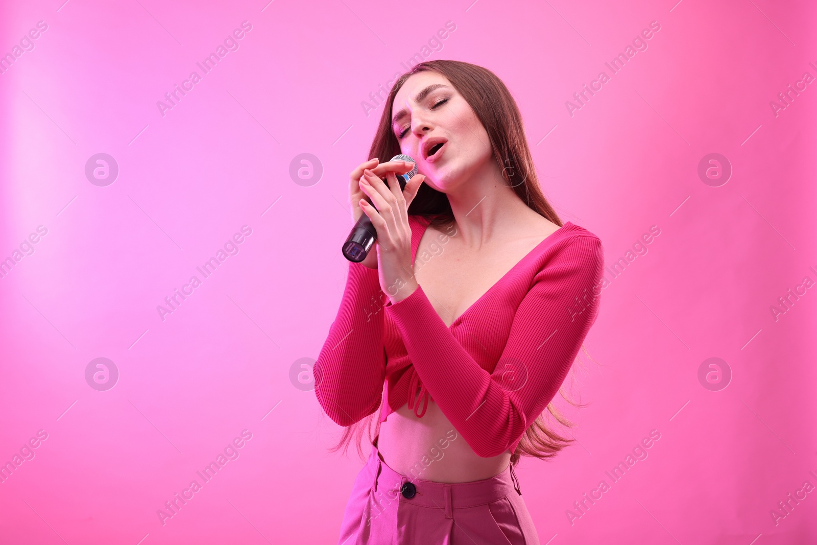 Photo of Emotional woman with microphone singing on pink background. Space for text