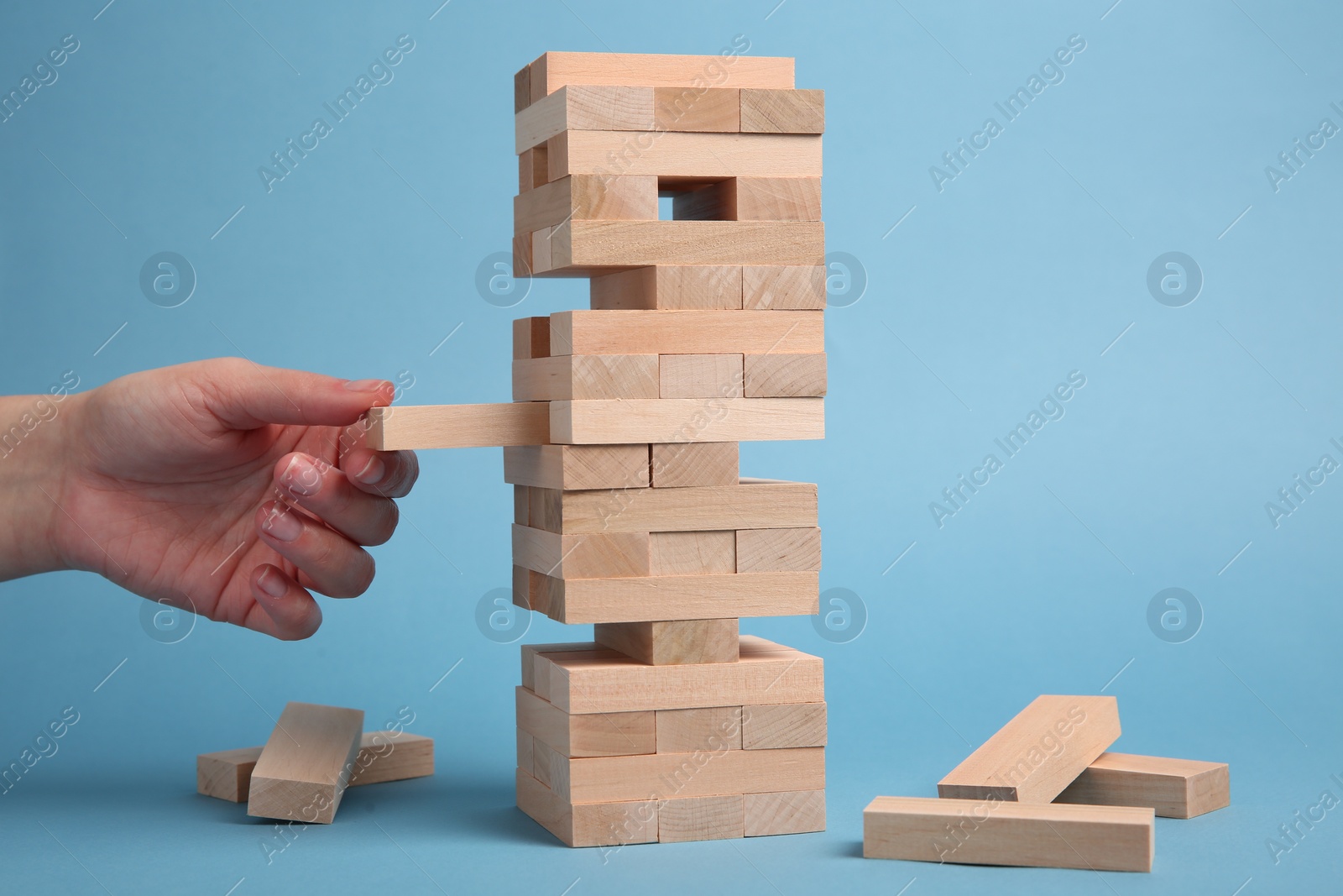 Photo of Woman playing Jenga on light blue background, closeup