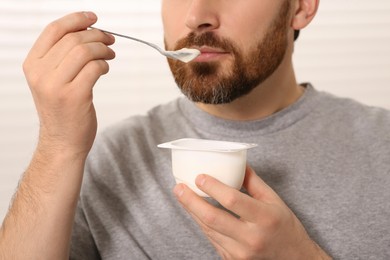 Man eating delicious yogurt indoors, closeup view