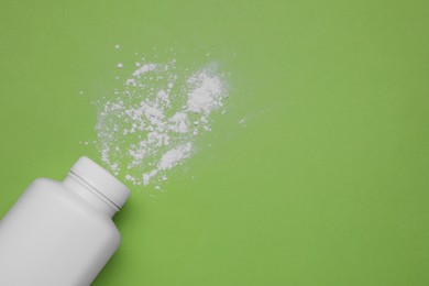 Photo of Bottle and scattered baby powder on green background, top view. Space for text