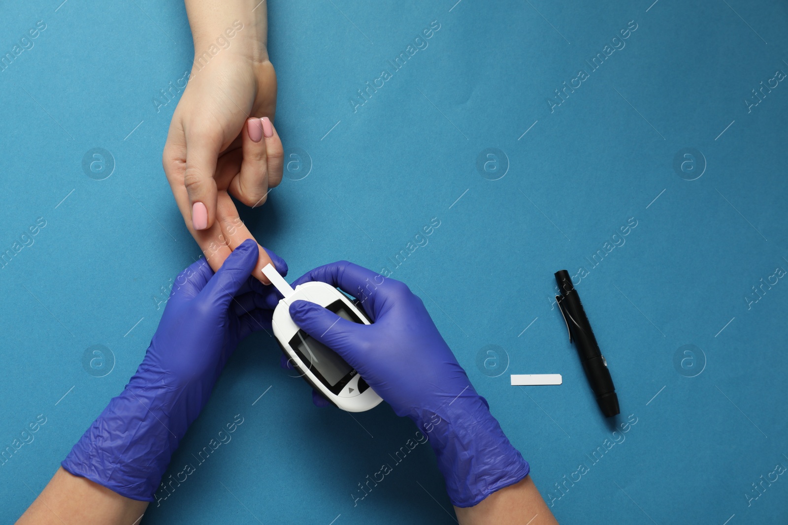 Photo of Diabetes. Doctor checking patient's blood sugar level with glucometer on blue background, top view