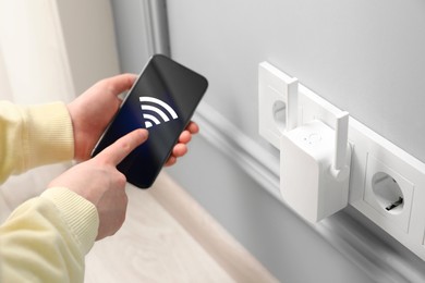 Woman with smartphone connecting to internet via wireless repeater indoors, closeup. Wi-Fi symbol on device screen