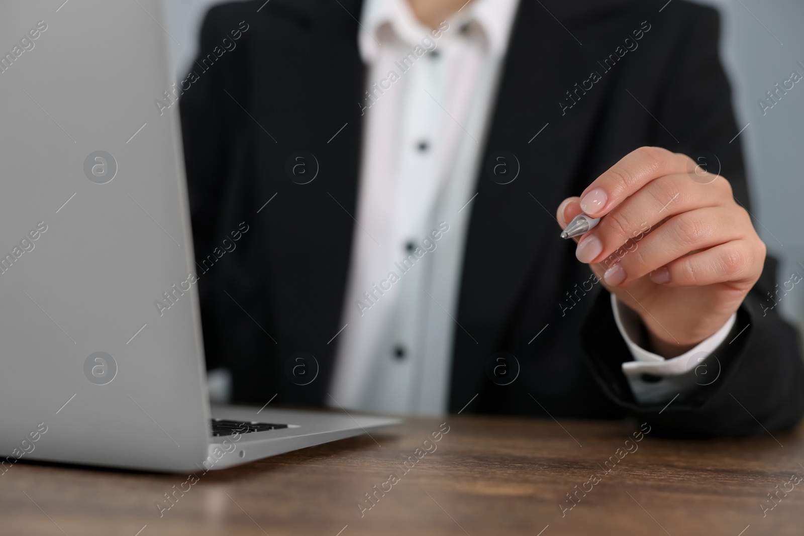 Photo of Woman with pen working on laptop at wooden table, closeup. Electronic document management