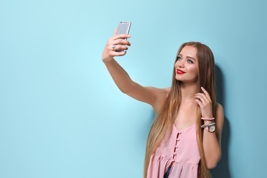 Photo of Attractive young woman taking selfie on color background