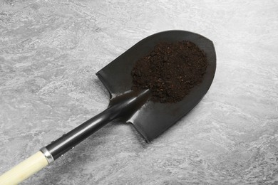 Photo of Metal shovel with fertile soil on gray textured surface, top view
