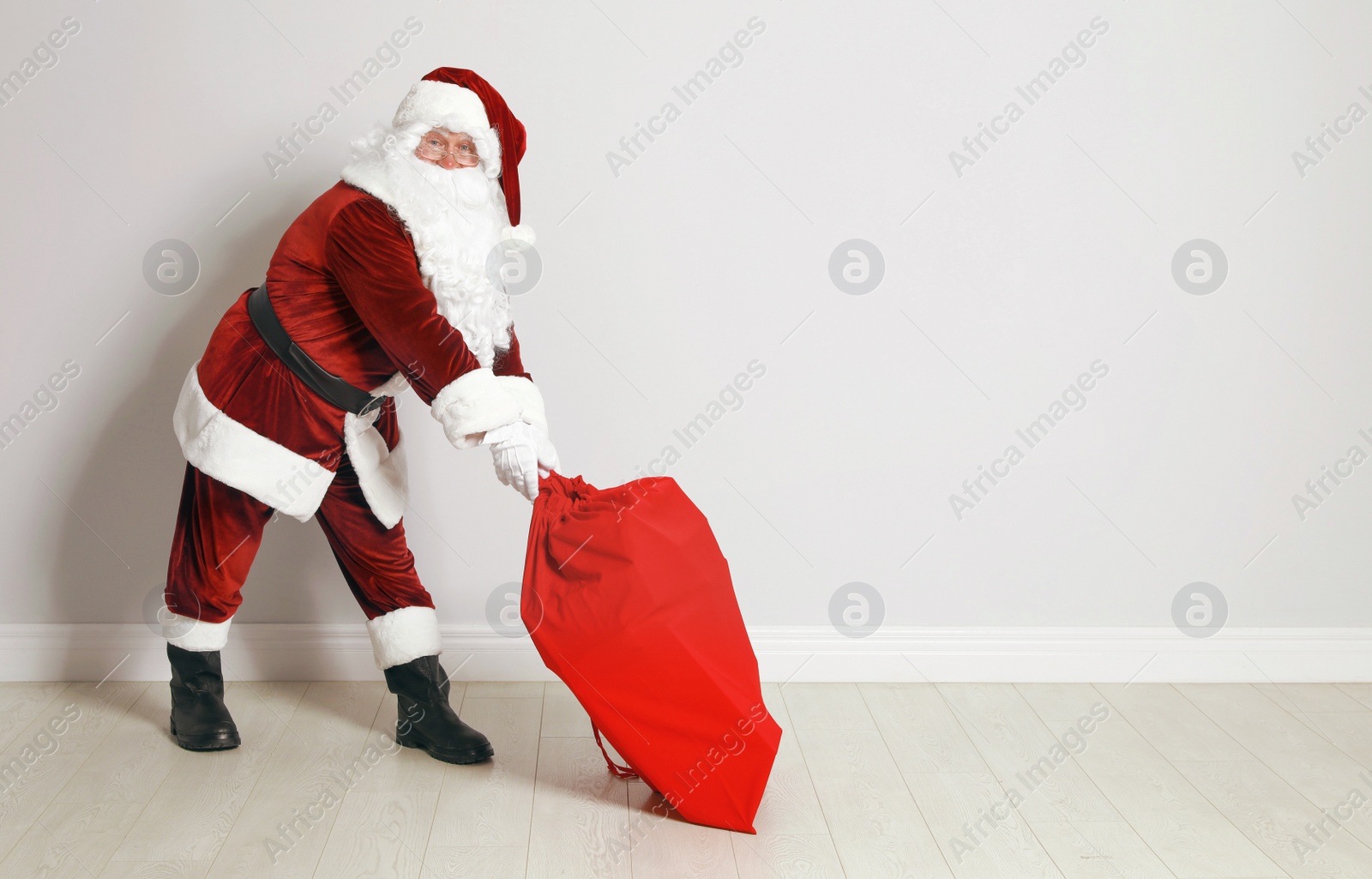 Photo of Authentic Santa Claus with bag full of gifts against grey wall. Space for text