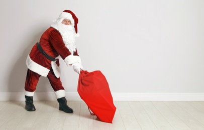 Photo of Authentic Santa Claus with bag full of gifts against grey wall. Space for text