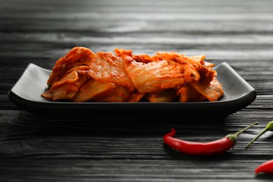Photo of Delicious kimchi with Chinese cabbage and red chili peppers on black wooden table