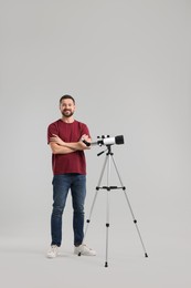 Happy astronomer with telescope on light grey background