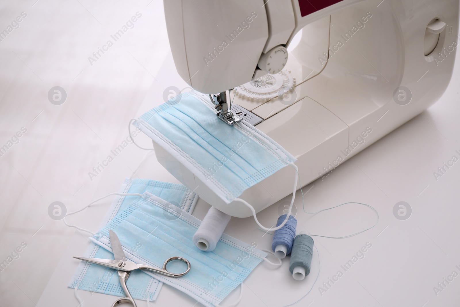 Photo of Sewing machine with disposable face mask on table, closeup