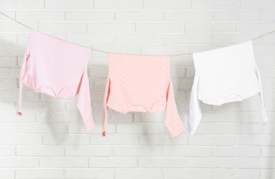 Baby clothes hanging on washing line near white brick wall