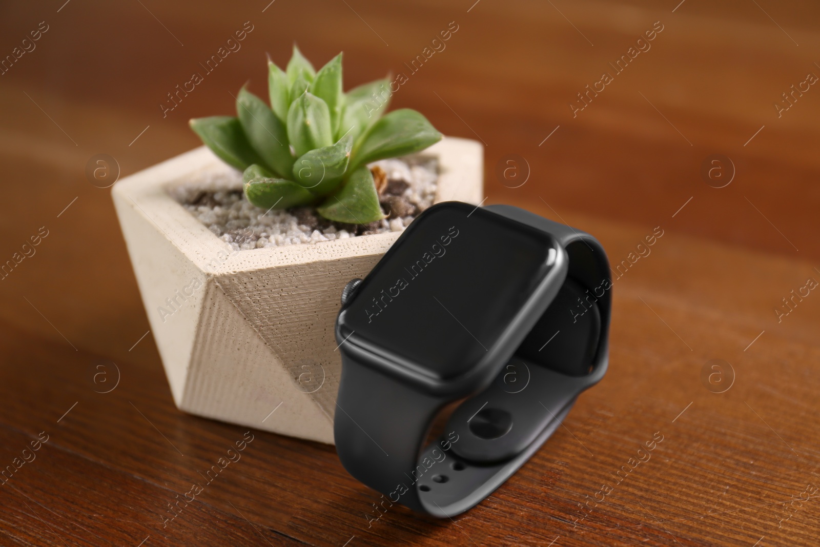 Stylish smart watch and plant on wooden table, closeup Photo of Stylish smart watch and plant on wooden table, closeup