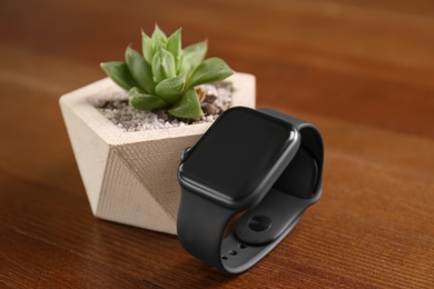 Photo of Stylish smart watch and plant on wooden table, closeup