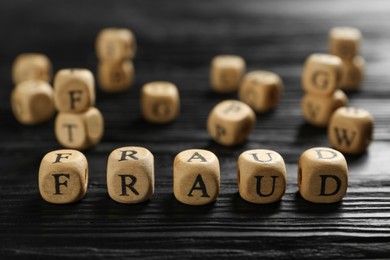 Photo of Word Fraud of cubes with letters on black wooden background