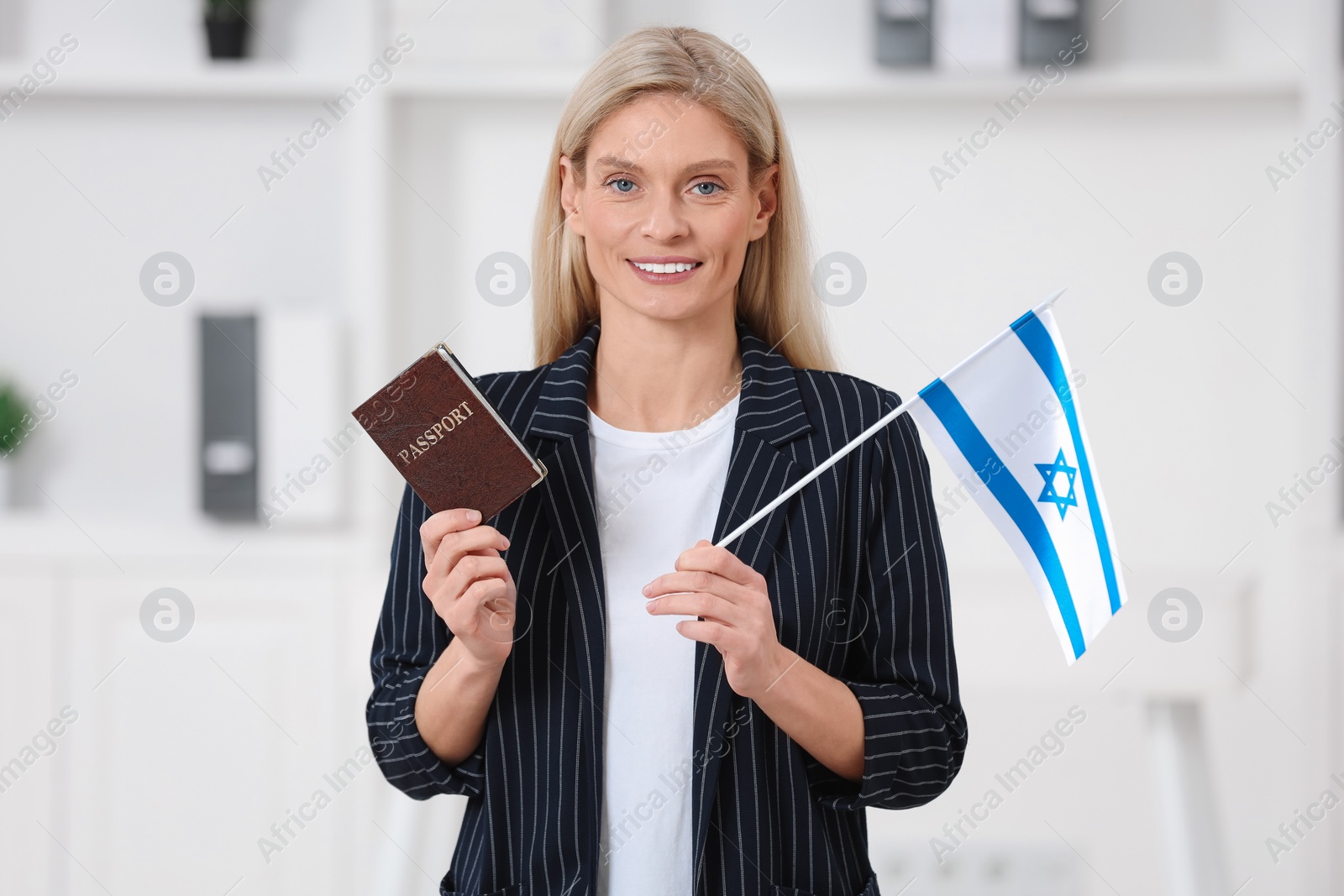 Photo of Immigration. Happy woman with passport and flag of Israel indoors