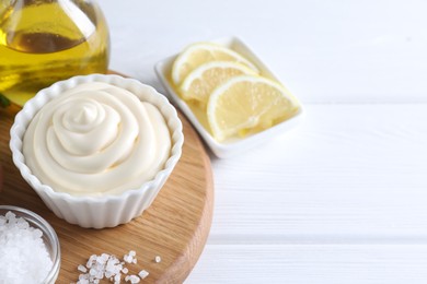 Fresh mayonnaise sauce in bowl and ingredients on white wooden table, closeup. Space for text