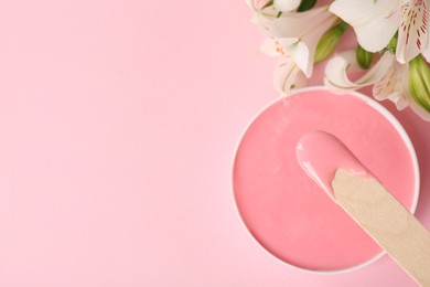 Photo of Wooden spatula, hot depilatory wax and flowers on light pink background, flat lay. Space for text