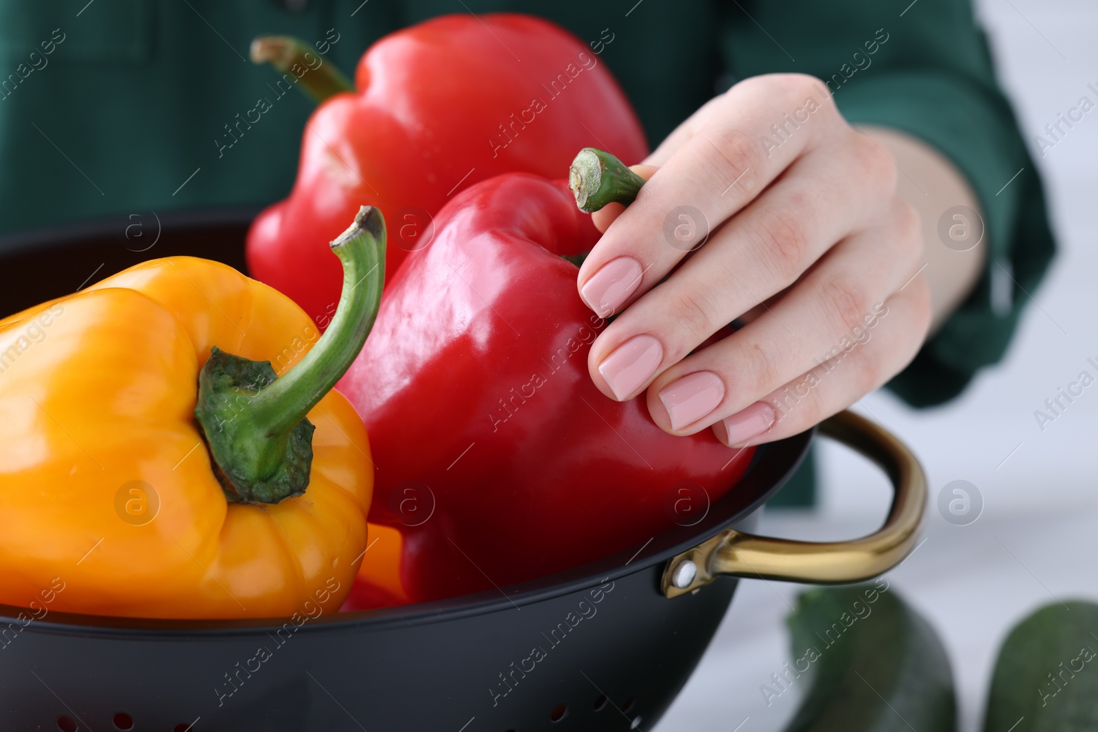 Photo of Woman taking bell pepper from black colander on blurred background, closeup