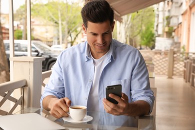 Photo of Man with cup of coffee and smartphone at outdoor cafe in morning