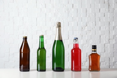 Bottles with different alcoholic drinks on table near white wall