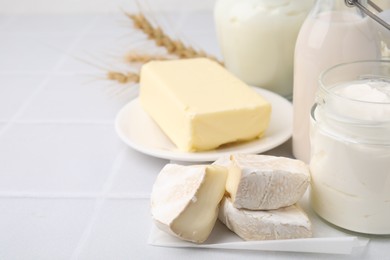 Different dairy products and spikes on white tiled table, space for text