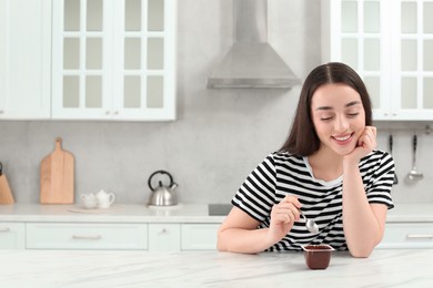 Photo of Happy woman with tasty yogurt in kitchen. Space for text