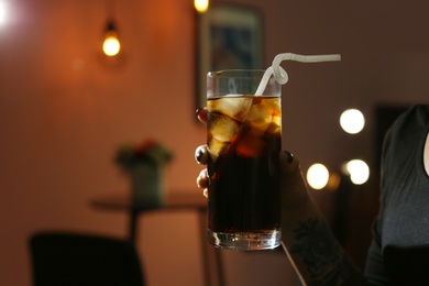 Woman with glass of cold cola in dark cafe, closeup. Space for text