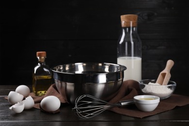 Photo of Making dough. Metal whisk and ingredients on dark wooden table