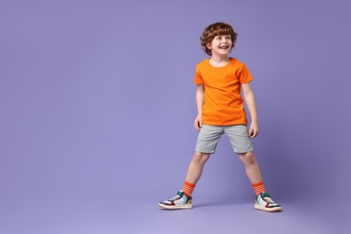 Photo of Happy little boy dancing on violet background. Space for text