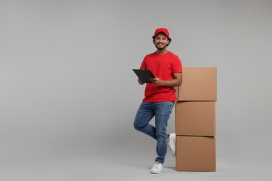 Photo of Happy courier with clipboard and stack of parcels on grey background, space for text