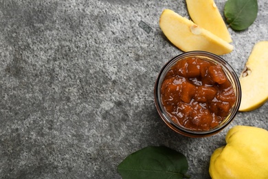 Photo of Delicious quince jam, fruits and leaves on grey table, flat lay. Space for text