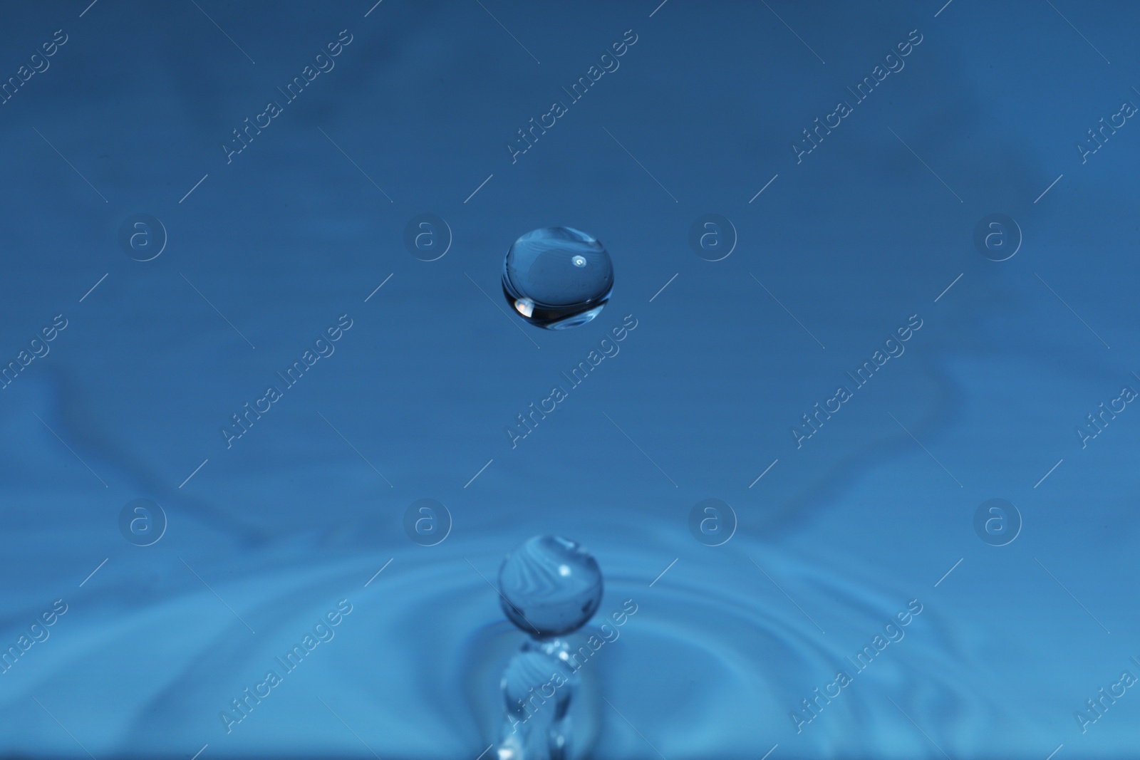 Photo of Drop falling into water on blue background, macro view