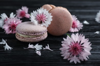 Photo of Delicious macarons and pink cornflowers on black wooden table