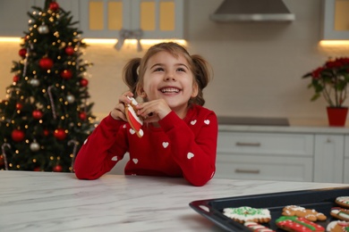 Cute little girl with freshly baked Christmas gingerbread cookie at table indoors