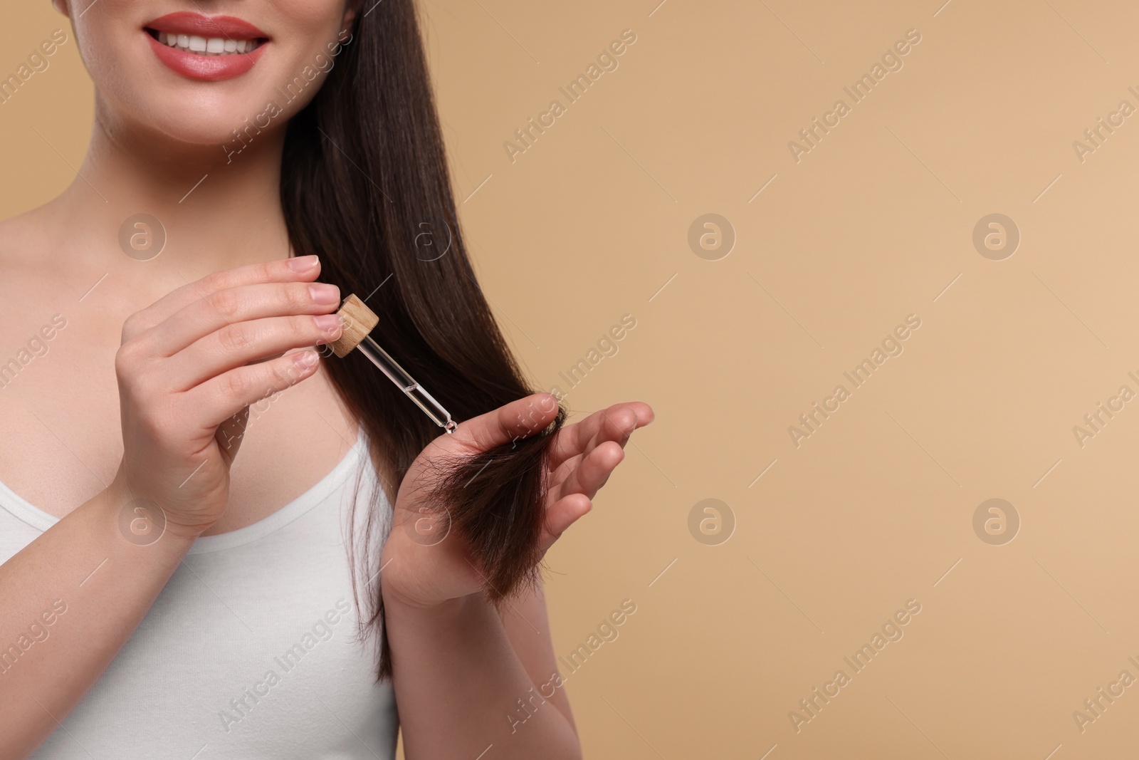 Photo of Happy woman applying essential oil onto hair on beige background, closeup and space for text