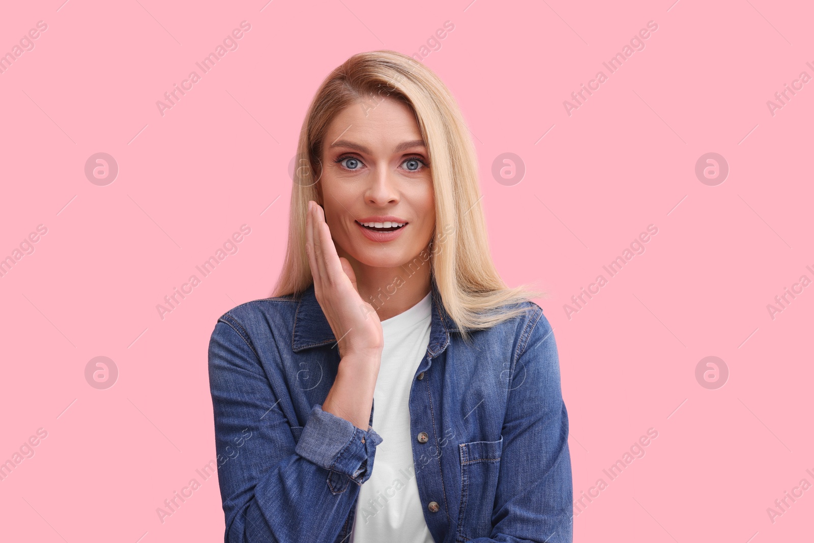 Photo of Portrait of surprised middle aged woman with blonde hair on pink background