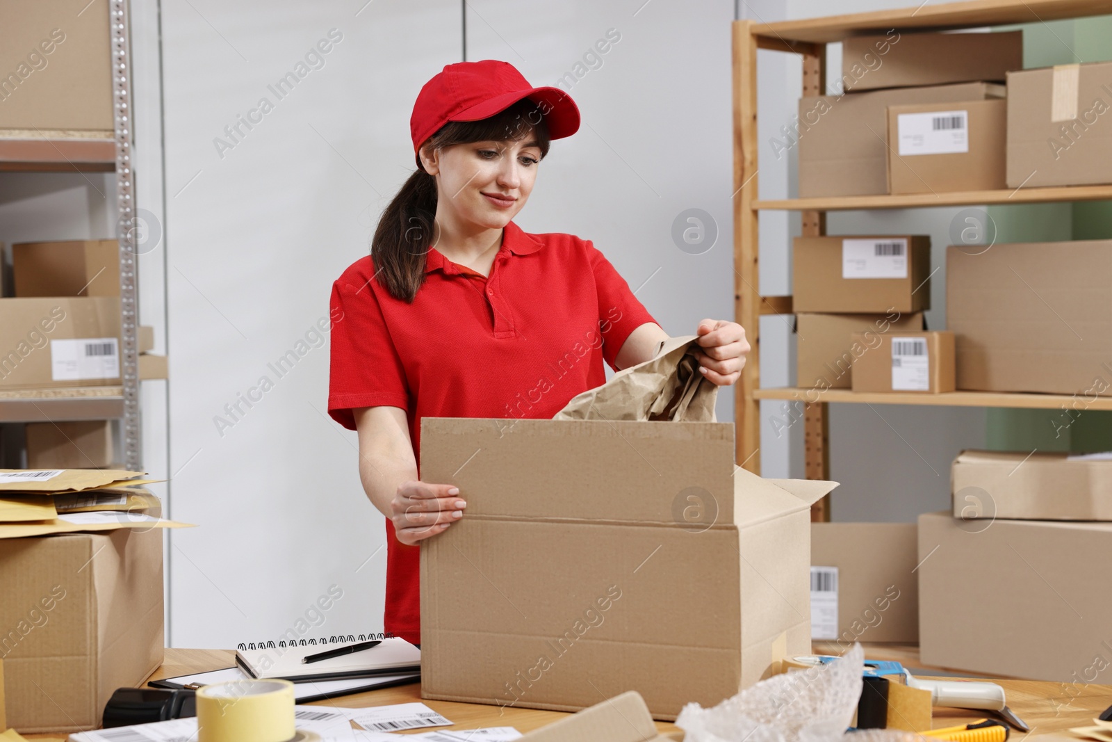 Photo of Post office worker packing parcel at wooden table indoors