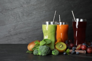 Photo of Delicious colorful juices in glasses and fresh ingredients on black table. Space for text