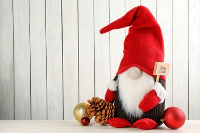 Photo of Cute Christmas gnome and festive decor on table against white wooden background. Space for text