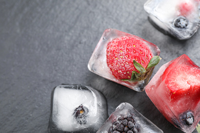 Ice cubes with different berries on dark grey table, closeup. Space for text
