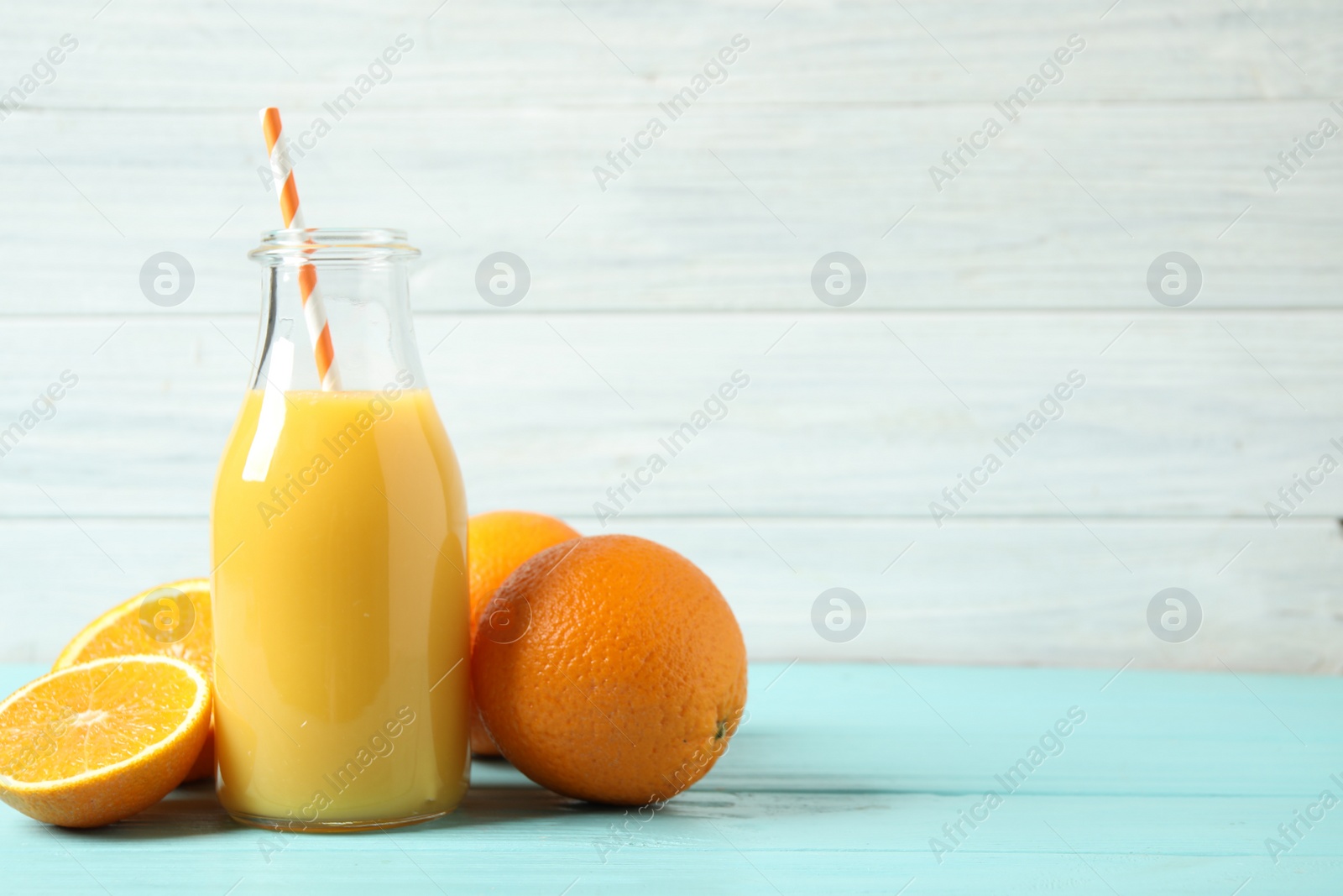 Photo of Bottle of orange juice and fresh fruits on light blue wooden table. Space for text