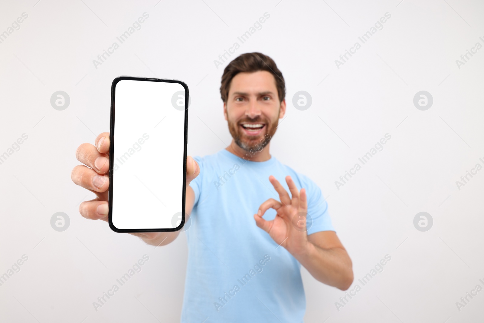 Photo of Handsome man showing smartphone in hand and OK gesture on white background, selective focus. Mockup for design