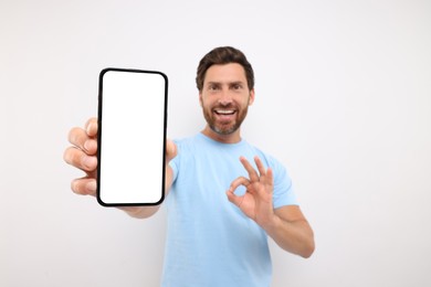 Handsome man showing smartphone in hand and OK gesture on white background, selective focus. Mockup for design