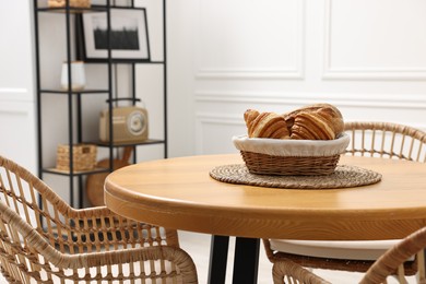 Photo of Tasty croissants on table and wicker chairs in dining room. Interior design