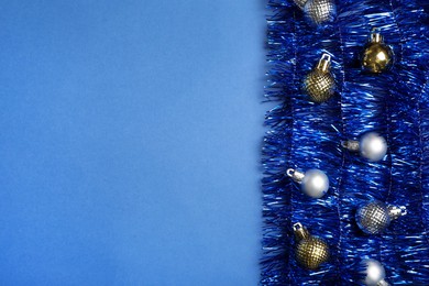 Photo of Bright tinsel and Christmas balls on blue background, flat lay. Space for text