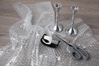 Photo of Candlesticks with bubble wrap, adhesive tape and scissors on wooden table