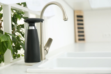 Photo of Modern automatic soap dispenser near sink in kitchen. Space for text